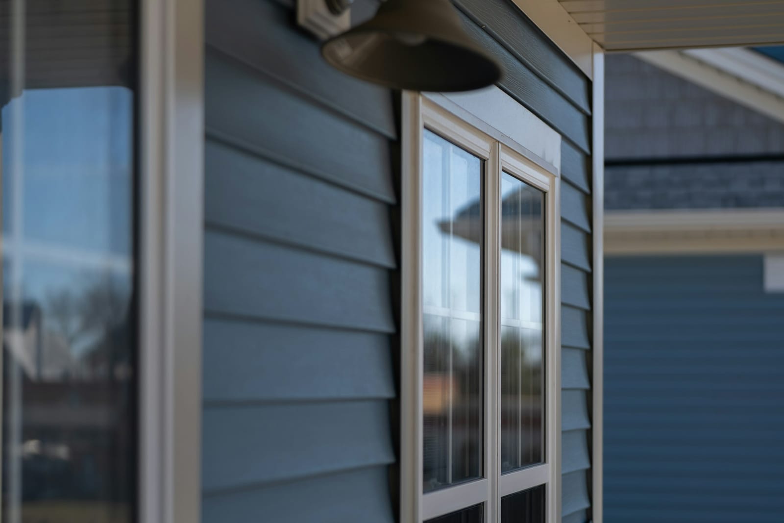 A white-framed window set in blue-grey lap siding, photographed from outside